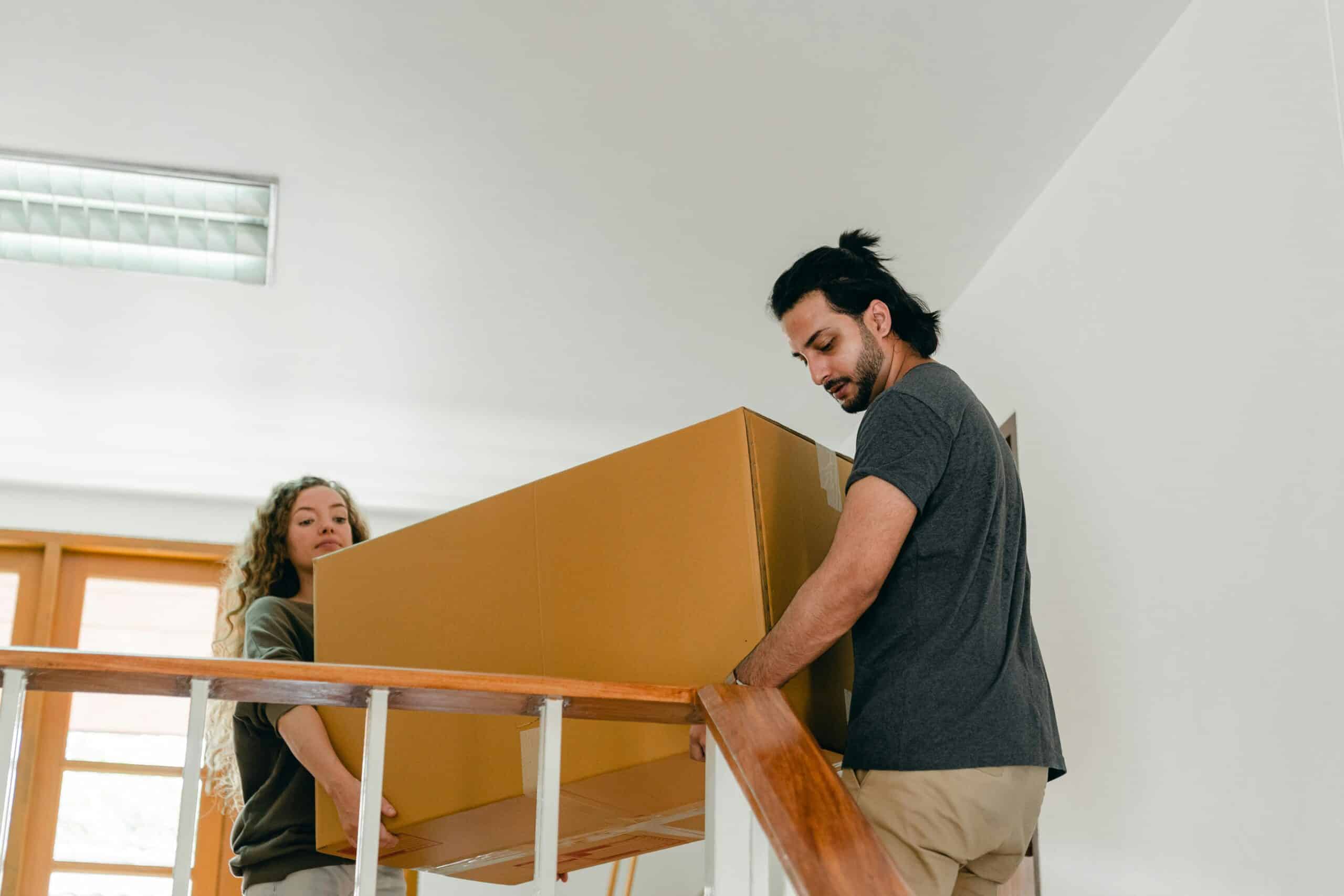 Couple carrying a sofa upstairs inside a bright home