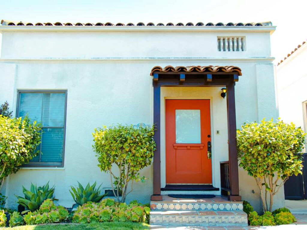 A white bungalow with a red front door and potted plants
